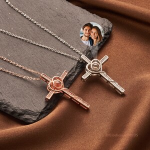 May include: Two silver and rose gold necklaces with cross pendants. Each pendant features a heart-shaped crystal that projects a photo when viewed from a certain angle. The photo shows a couple smiling at the camera.