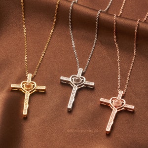 May include: Three silver cross necklaces with a heart-shaped pendant that projects an image when held up to a light source. The necklaces are available in gold, silver, and rose gold.