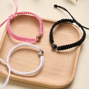 May include: Three friendship bracelets with black, white, and pink cords. Each bracelet has a small, round, silver charm with a black or clear stone.
