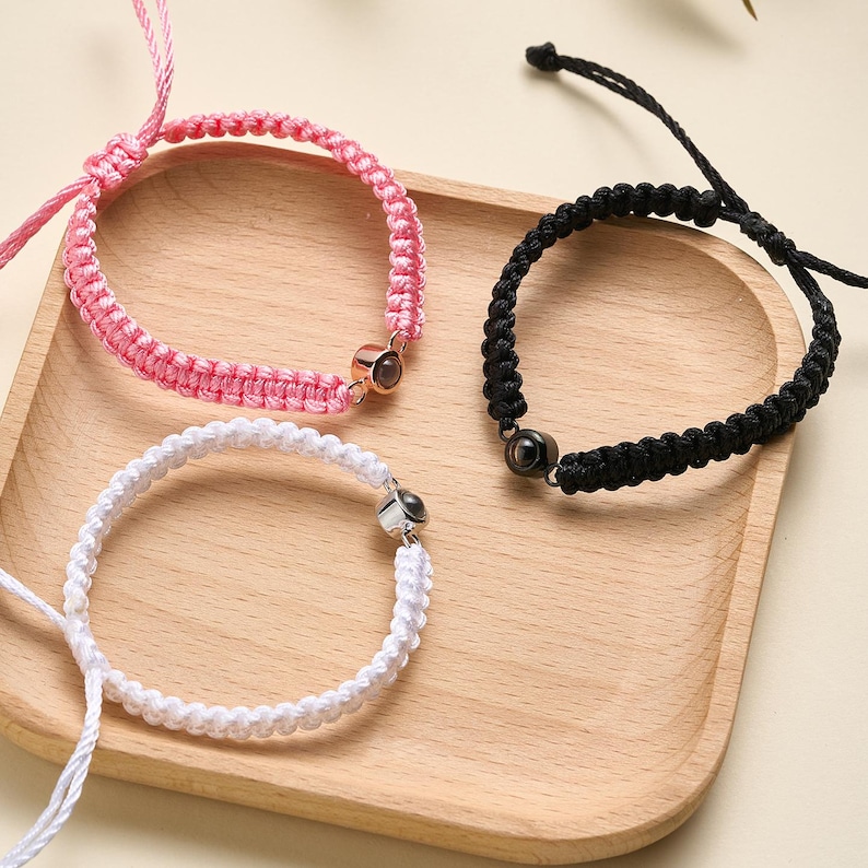 May include: Three friendship bracelets with black, white, and pink cords. Each bracelet has a small, round, silver charm with a black or clear stone.