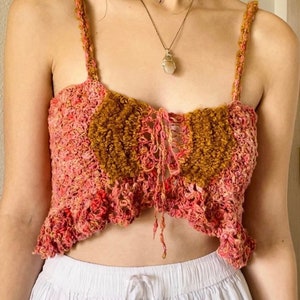 Könnte beinhalten: Ein gehäkeltes Crop-Top in Rosa und Braun. Das Top hat einen Schnürverschluss vorne und einen Rüschen-Saum.