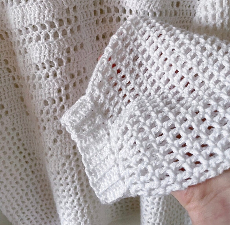 Puede incluir: Top blanco de crochet con tejido suelto y abierto. El top tiene un escote ancho y acanalado y mangas largas.