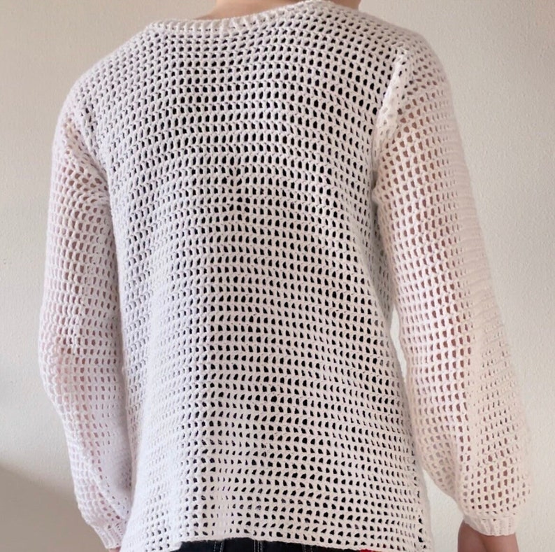 Puede incluir: Su&eacute;ter blanco de crochet con un corte holgado y mangas largas. El su&eacute;ter tiene un delicado patr&oacute;n de tejido abierto.