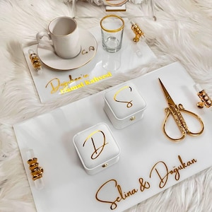May include: White serving trays with gold accents, a teacup, a small glass, and two white boxes with gold lettering. The trays have gold handles and decorative gold scissors. The text "Selina & Doğukan" is visible.