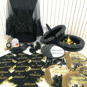 May include: A black bridal veil with lace trim, a matching basket, and decorative items. Several black fabric squares feature the gold text Mürvet & Abdullah, while circular gold-trimmed fans display the text Mürvet'in Kına Gecesi.