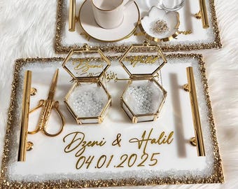 May include: Two white trays with gold trim and handles. Each tray holds a teacup, saucer, and small dish. The bottom tray has two hexagonal glass boxes and gold scissors. The trays are decorated with gold script and a date.
