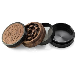 May include: A four-piece wooden and black metal grinder with a circular design. The top piece has a wood grain pattern and a logo with the letter "Q".