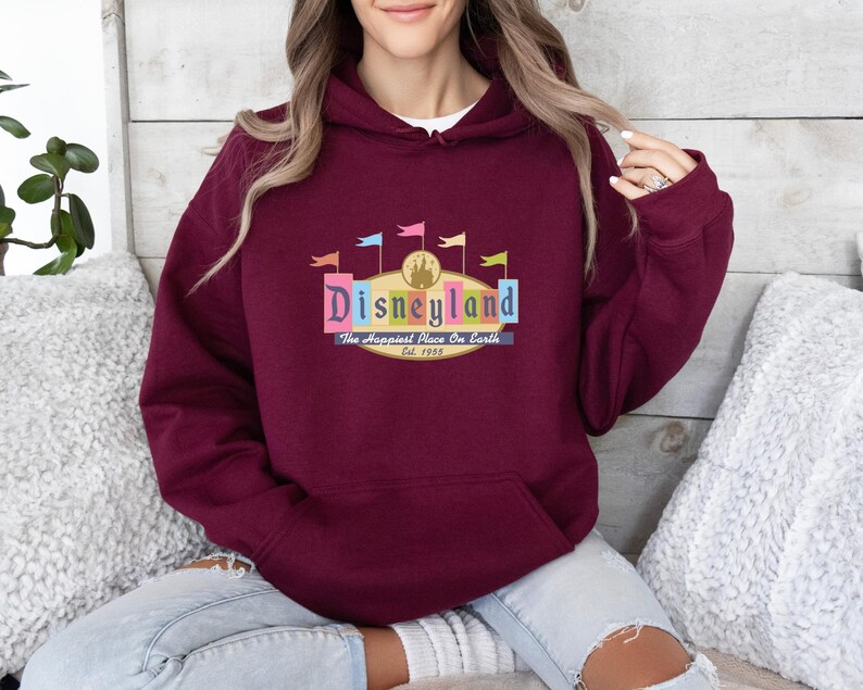 A woman wearing a burgundy hoodie with a Disneyland logo is sitting on a couch.