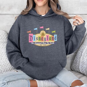 A woman wearing a gray hoodie with a Disneyland logo and text, sitting on a couch.