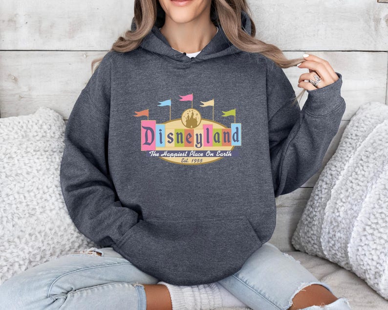 A woman wearing a gray hoodie with a Disneyland logo and text, sitting on a couch.