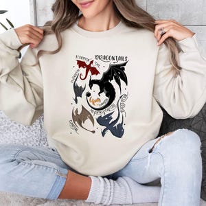 May include: A cream-colored sweatshirt with a graphic of five dragons with different colored tails and the text "Dragontails" in black lettering.