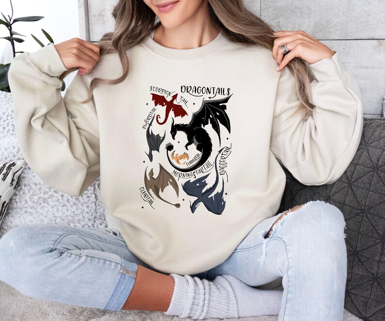 May include: A cream-colored sweatshirt with a graphic of five dragons with different colored tails and the text "Dragontails" in black lettering.