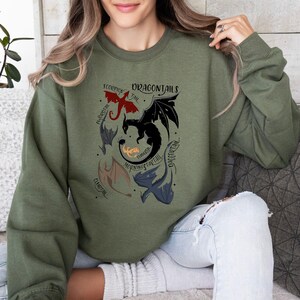 May include: A green sweatshirt with a graphic of five dragons with different names: "Scorpion Tail", "Embertail", "Morning Startail", "Thunder", and "Dragontail".