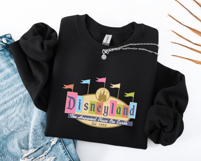 A black sweatshirt with a colorful graphic of Disneyland printed on it, along with a denim skirt and a necklace.
