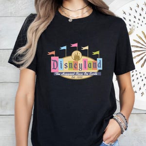 A woman wearing a black t-shirt with a colorful graphic of Disneyland and text that says "Disneyland The Happiest Place on Earth Est. 1955".