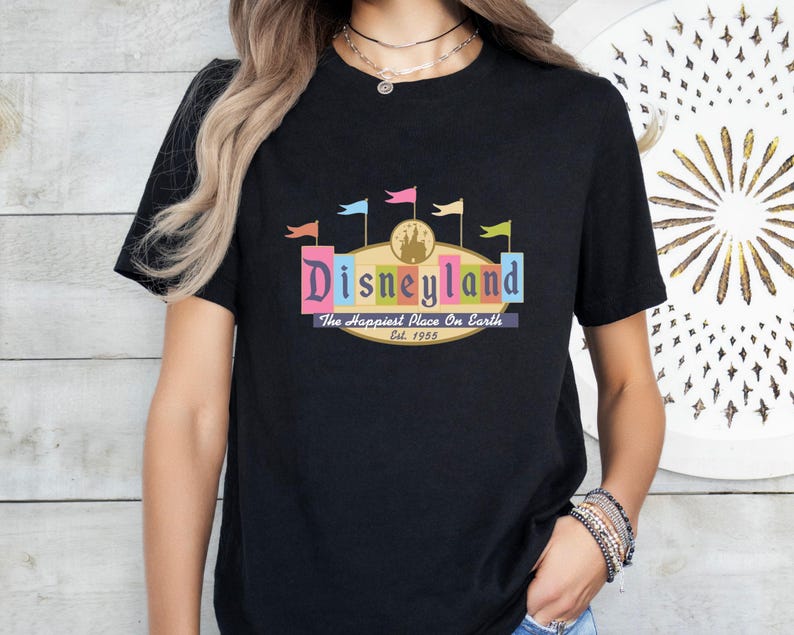 A woman wearing a black t-shirt with a colorful graphic of Disneyland and text that says "Disneyland The Happiest Place on Earth Est. 1955".