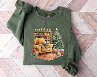 May include: A dark green sweatshirt featuring a cozy Christmas scene. A gingerbread man reads in a chair near a Christmas tree and bookshelf. Presents are scattered around the rug. The sweatshirt is made of a soft material.