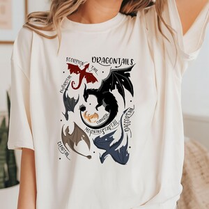 May include: White t-shirt with a graphic of different dragon tails. The tails are labeled with names like "Dragontail", "Morningstarttail", "Daggertail", "Flametail", "Clubtail", "Scorpian Tail", and "Icecrystal".