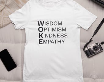 May include: White t-shirt with the word "WOKE" spelled out vertically, with each letter representing a word: Wisdom, Optimism, Kindness, and Empathy. A black smartphone and a vintage camera are also visible.