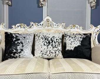 May include: Three black and white cowhide throw pillows on a white and gold ornate sofa. The sofa has a cream colored fabric with a diamond pattern.