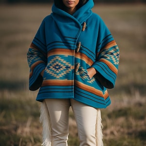 May include: A turquoise hooded poncho with a Southwestern pattern in orange, brown, and cream. The poncho has wooden toggle closures and is paired with cream-colored pants, brown cowboy boots, and a cowboy hat.