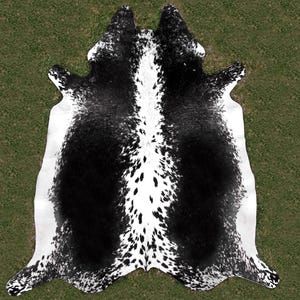 May include: Black and white cowhide rug with a spotted pattern. The rug is laid out on a green grassy surface.