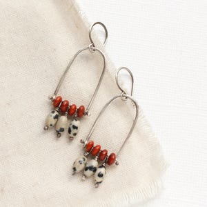 May include: A pair of silver hoop earrings with a dangling cluster of red and white dalmatian jasper beads.