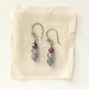 May include: A pair of drop earrings featuring silver-toned ear wires and a vertical arrangement of three faceted beads. Each earring includes a small deep pink bead at the top, a translucent grey bead in the center, and a larger light purple bead at the base.