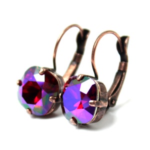 May include: A pair of leverback earrings featuring round, iridescent purple and red crystals. The crystals are set in a copper-colored metal frame. The earrings are displayed against a white background.