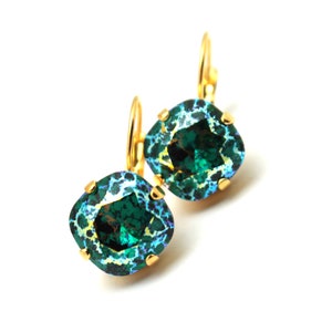 May include: A pair of gold earrings with emerald green square-shaped stones. The stones have a blue and green iridescent finish.