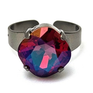 May include: A silver ring featuring a large, faceted, red and purple gemstone.
