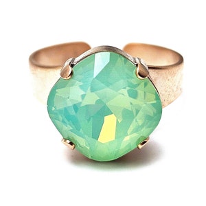 May include: A ring with a large, light green, faceted gemstone set in a gold-toned band.