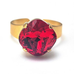 May include: A gold ring featuring a large, red, faceted gemstone.