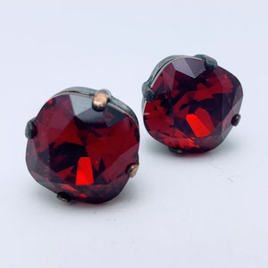 Op de afbeelding: Een paar rode edelsteen oorbellen met zilveren instellingen. De oorbellen zijn klein en hebben een facetgeslepen ontwerp.