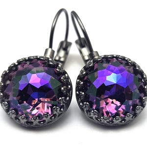 May include: A pair of round drop earrings featuring faceted purple and iridescent crystals set in dark gunmetal settings with a crown-like edge and lever-back closures. The crystals display deep violet hues with flashes of blue and pink light.