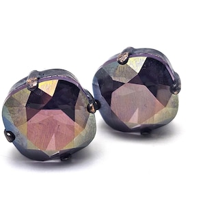 Pode incluir: Um par de brincos de pressão facetados e iridescentes. Os brincos têm uma moldura metálica escura e uma aparência multicolorida, semelhante a uma gema, com tons de roxo, dourado e verde. Em um fundo branco.