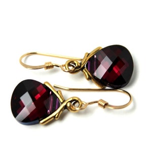 Op de afbeelding: Een paar gouden oorbellen met hangende traanvormige rode edelstenen. De oorbellen hebben een delicaat, ingewikkeld ontwerp.