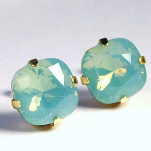 May include: A pair of gold stud earrings with square-shaped, light blue opal stones.