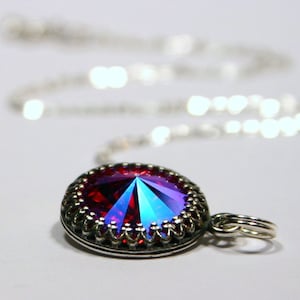 Peut inclure: Un collier en chaîne argent avec un pendentif en cristal iridescent rouge et bleu. Le pendentif est serti dans une bélière argentée avec une bordure décorative.