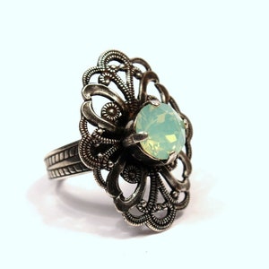 May include: A silver ring with a delicate filigree design and a pale green gemstone in the center.