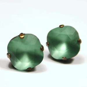Può includere: Un paio di orecchini in vetro verde con accenti dorati. Gli orecchini sono rotondi e hanno un design sfaccettato.