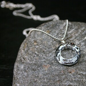 May include: A silver chain necklace with a clear crystal pendant in the shape of a circle. The pendant is made of faceted crystal and has a wire wrapped around the edge.