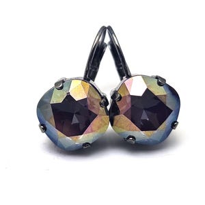May include: A pair of leverback earrings with iridescent, faceted, square-shaped crystals. The crystals reflect a spectrum of colors, including blue, yellow, and purple. The earring settings and leverbacks are a dark gunmetal color.