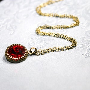 Peut inclure: Un collier en chaîne dorée avec un pendentif en pierre rouge. Le pendentif est rond et a une bordure dorée.