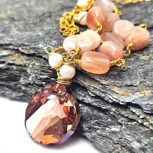Puede incluir: Un collar de oro con un gran colgante de cristal facetado de color melocotón. El collar está hecho con una cadena de oro y presenta cuentas de color melocotón y blancas.