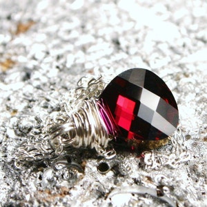 May include: A silver chain necklace with a dark red faceted crystal pendant. The crystal is wrapped in silver wire.