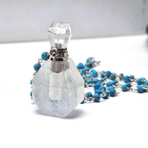 Könnte beinhalten: Ein klarer, facettierter Glasparfümflakon mit silberfarbenem Verschluss und einer türkisfarbenen Perlenkette. Die Flasche hat eine geometrische Form und ist mit einer hellen Flüssigkeit gefüllt.