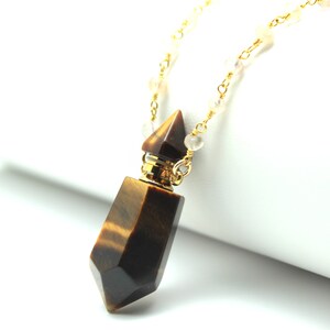 May include: A gold chain necklace with a brown and gold tiger's eye crystal pendant. The pendant is shaped like a bottle with a gold stopper.