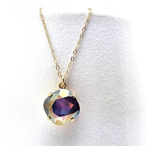 May include: A gold-tone necklace featuring a large, iridescent pendant. The pendant has a rounded square shape with a purple centre and a shimmering, multi-coloured surface. The necklace is shown against a white backdrop.