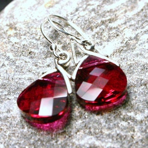 Könnte beinhalten: Ein Paar silberne Ohrhänger mit tropfenförmigen roten Kristallsteinen.